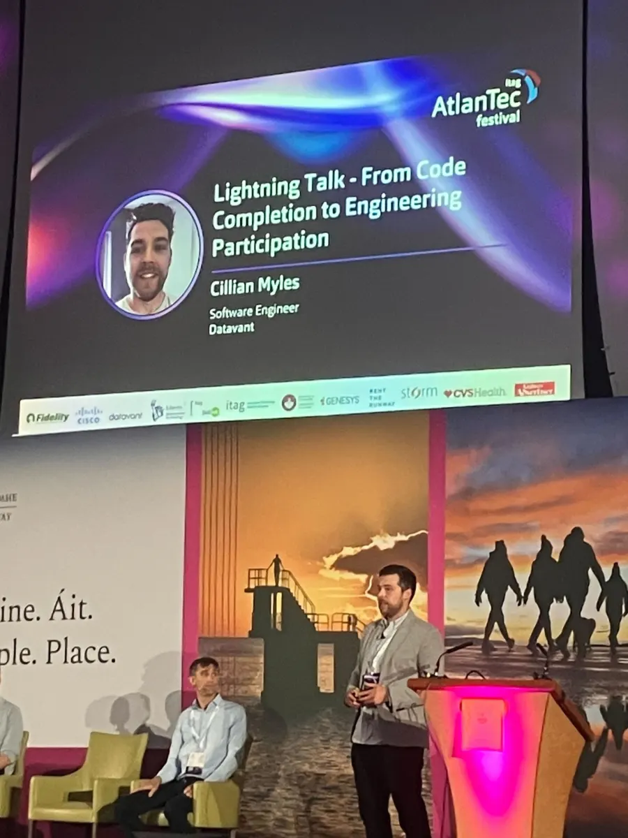 Cillian on stage beneath the title slide, Lightning Talk: From Code Completion to Engineering Participation